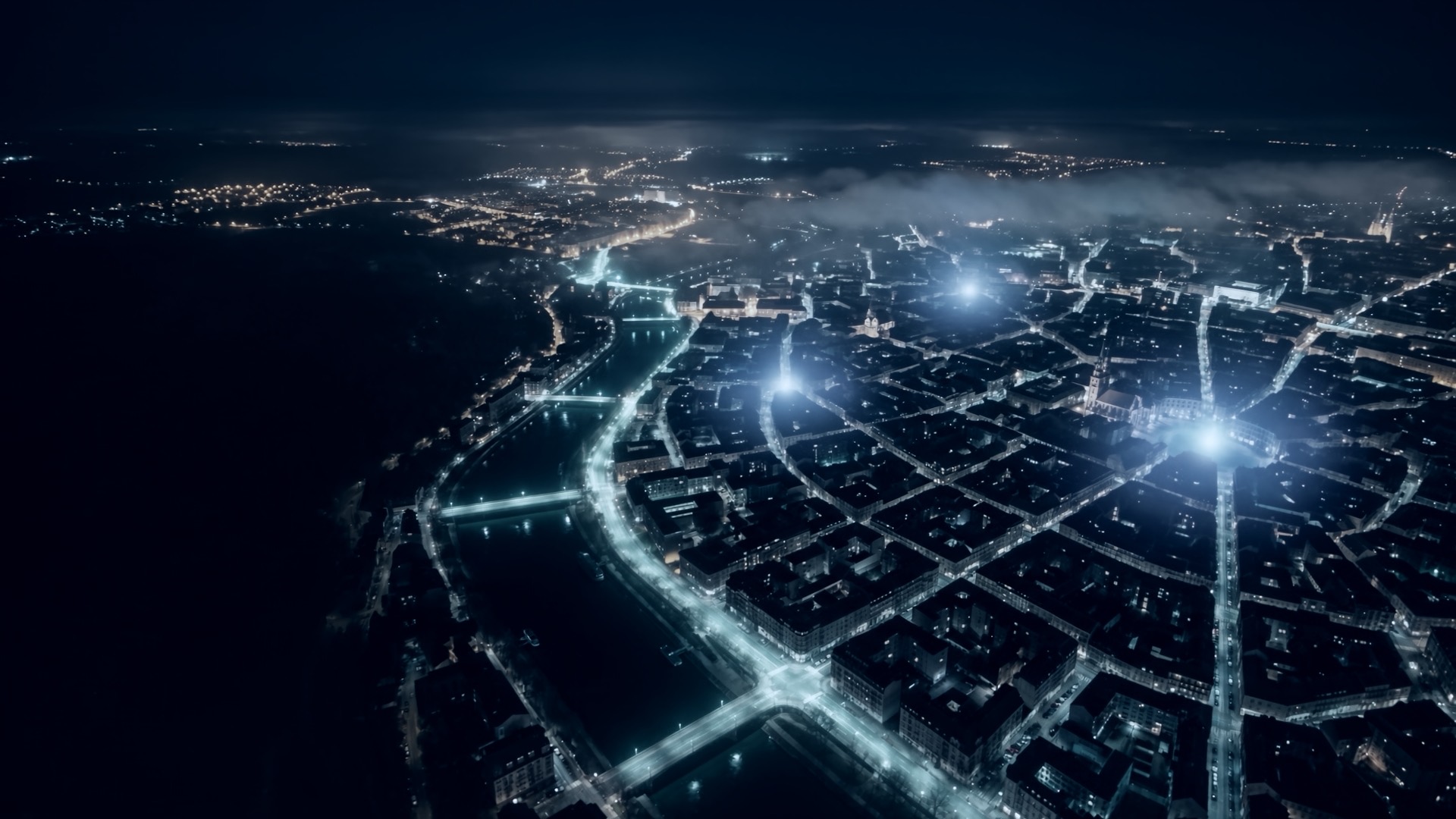 Aerial night view of a city along a river, with the main roads lit and glowing points marking the stations that cover it